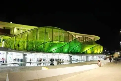 El Pabell&oacute;n de Am&eacute;rica Latina cambia espectacularmente de imagen del d&iacute;a a la noche. Un verde &aacute;cido, casi fluorescente, anima el exterior de este edificio.
Por Gonzalo Baz&aacute;n y Pilar Artiaga