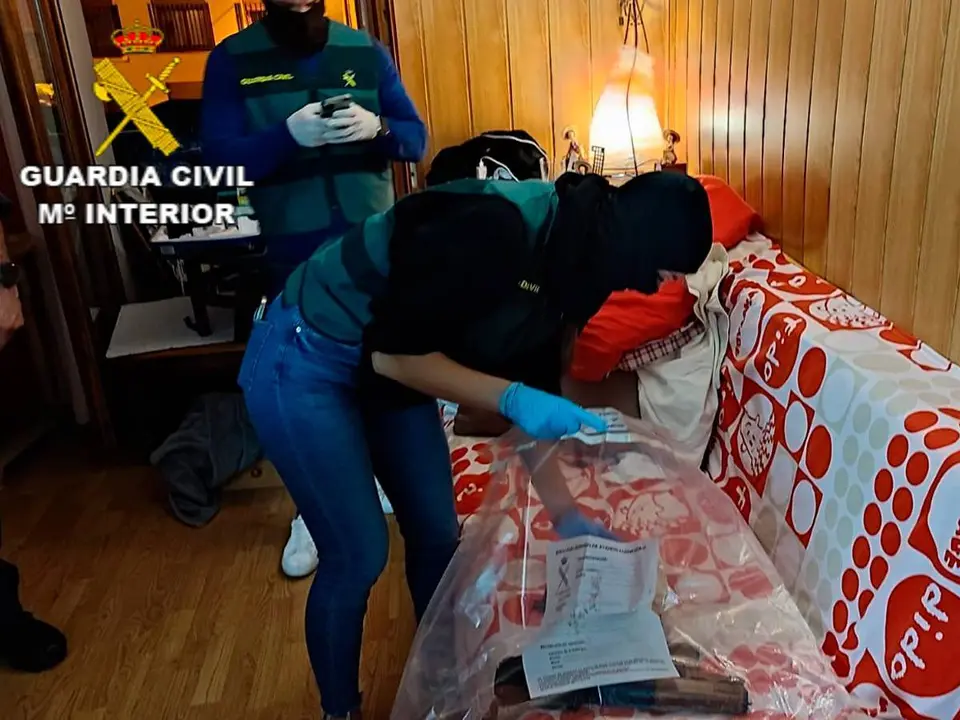 Un polic&iacute;a pone en una bolsa varias armas desde un sof&aacute; en la casa del terrorista