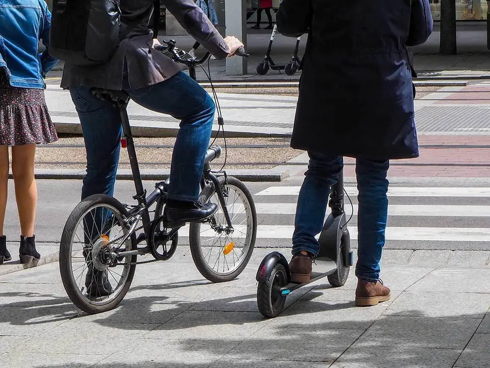 Usuarios de bicicleta y patinete esperan en un paso de cebra