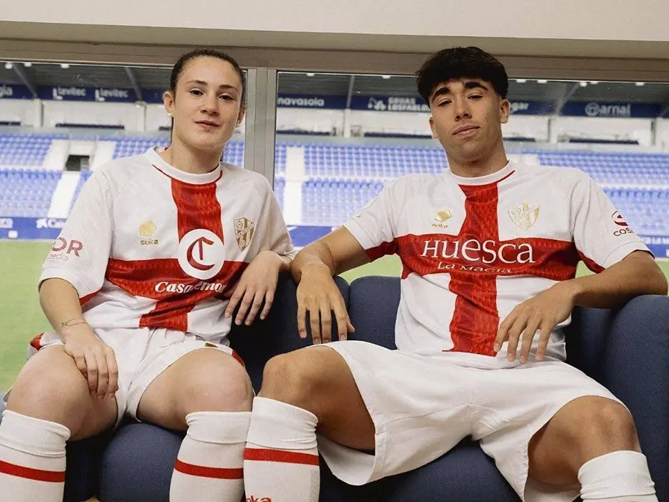 Dos j&oacute;venes posan con la nueva equipaci&oacute;n sentados en un sof&aacute;