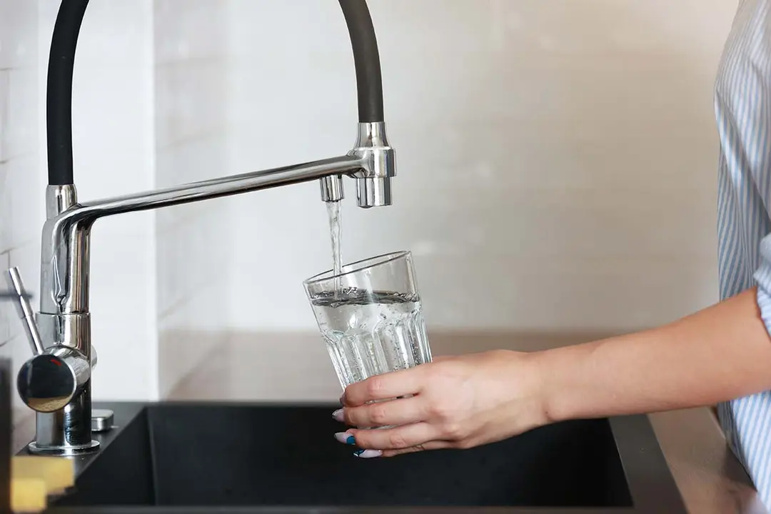 Persona cogiendo agua de un grifo en un vaso 