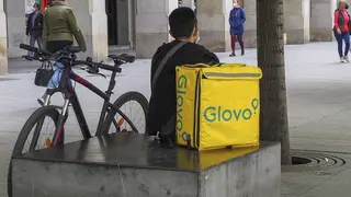 repartidor de glovo sentado junto a una bicicleta