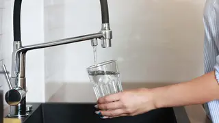 Persona cogiendo agua de un grifo en un vaso 