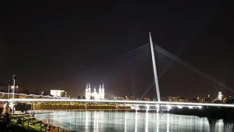A orillas del Ebro, los visitantes contemplan una espectacular panor&aacute;mica de la Pasarela del Voluntariado. Al fondo, el Pilar no pierde su protagonismo y, con sus focos, parece saludar al cielo.
Por Gonzalo Baz&aacute;n y Pilar Artiaga