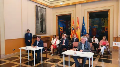 El alto comisionado y el comisionado aragon&eacute;s de la infancia firmando el acuerdo de adhesi&oacute;n a la alianza en una sala del edificio Pignatelli. Detr&aacute;s, varios consejeros y administrativos sentados.