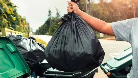 Una persona arroja una bolsa de basura a un contenedor