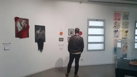 Un hombre viendo la exposici&oacute;n, varias piezas de arte textil en el fondo