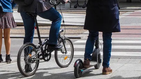 Usuarios de bicicleta y patinete esperan en un paso de cebra