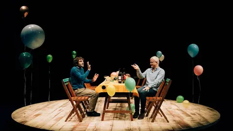 Dos actores sentados a una mesa con globos