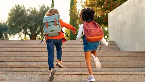Dos escolares de espaldas yendo al colegio
