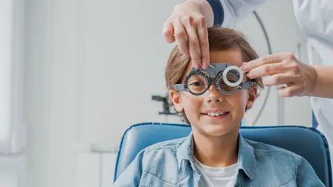 Ni&ntilde;o con gafas comprueba la visi&oacute;n ocular en el oftalm&oacute;logo pedi&aacute;trico