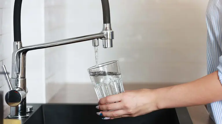 Persona cogiendo agua de un grifo en un vaso 