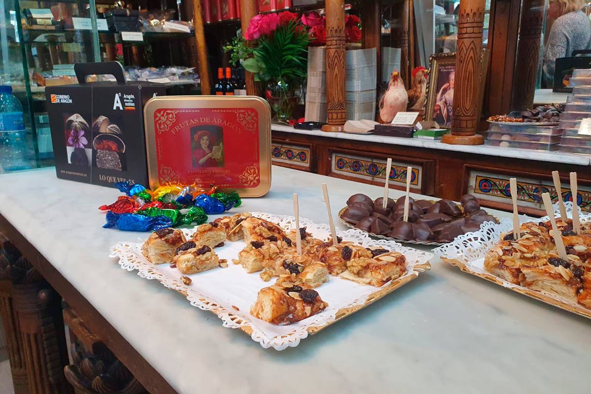 El escaparate de una tienda con dos bandejas de trenza de almendras y pasas. una de frutas de Aragón, una caja de frutas de metal y decoración de Aragón Alimentos Nobles
